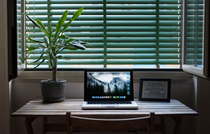 Elegant home office desk setup with a laptop and a plant near a window. Ideal for remote work.