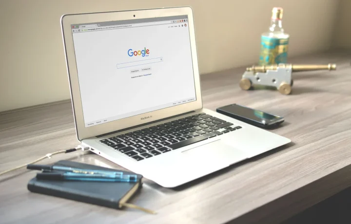 Espaço de trabalho organizado com laptop mostrando busca no Google, smartphone e caderno sobre mesa de madeira