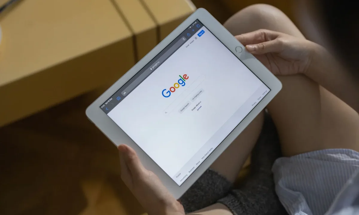 Mãos segurando um tablet exibindo a página de busca do Google, representando a otimização de SEO com IA