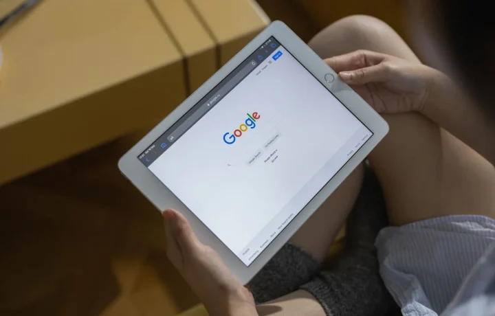 Mãos segurando um tablet exibindo a página de busca do Google, representando a otimização de SEO com IA