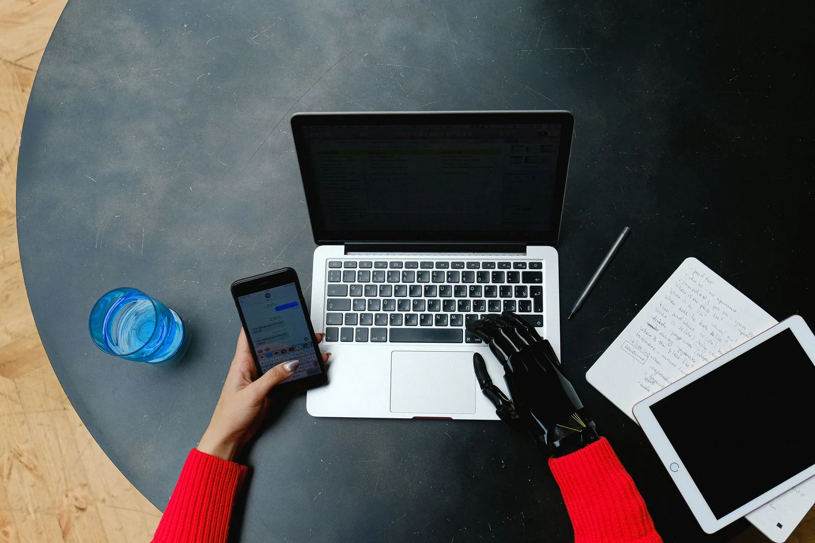 Prosthetic hand operating a laptop, smartphone and tablet, showing the connected tools of an automated content workflow