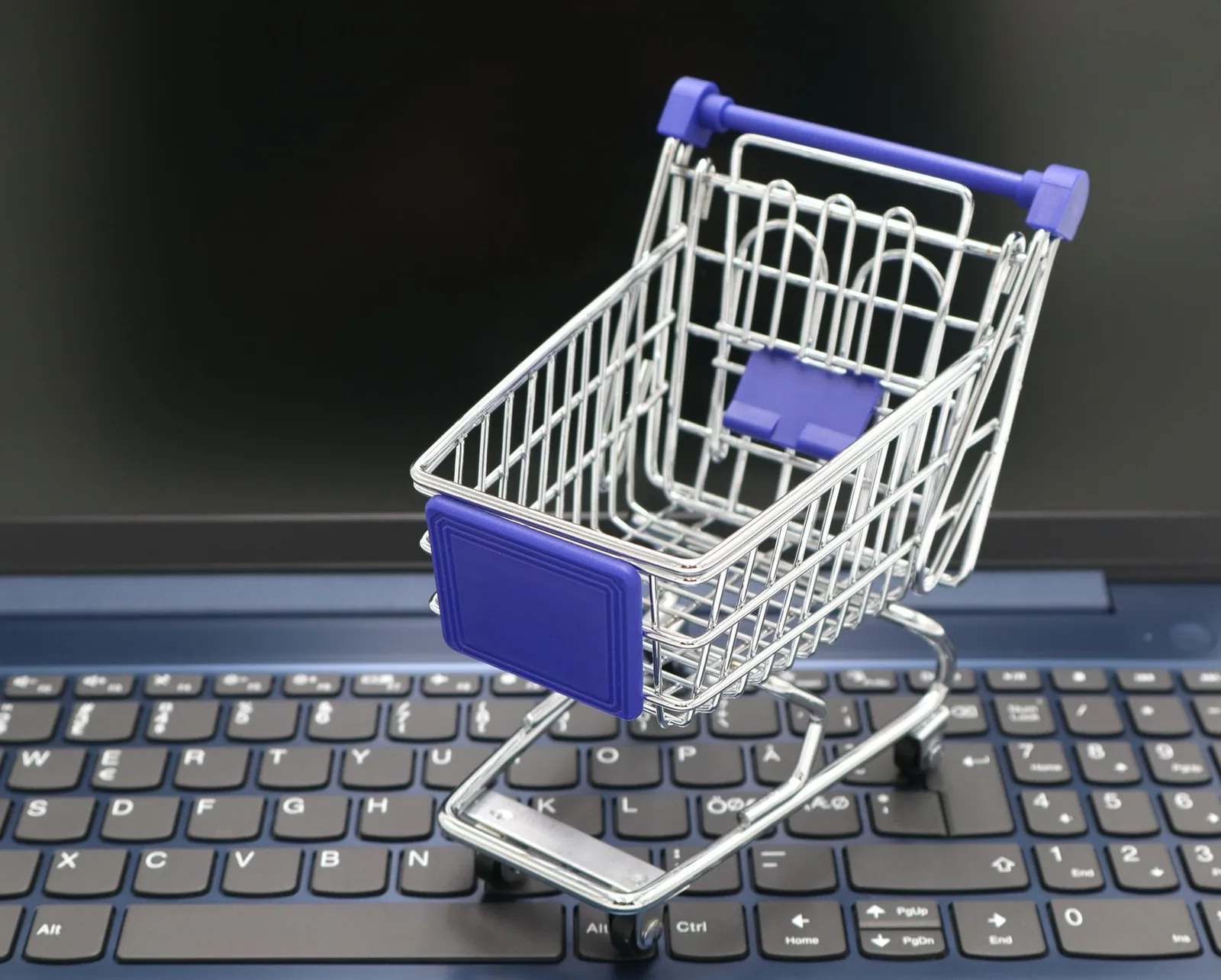 Carrinho de compras em miniatura sobre o teclado de notebook, representando o comércio digital