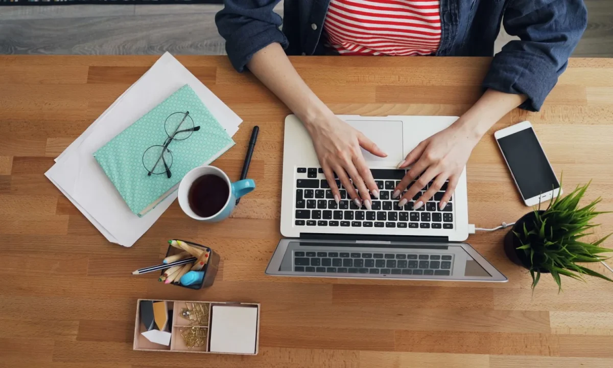 Hands typing on a laptop at a tidy wooden desk, a key step in blog authority building
