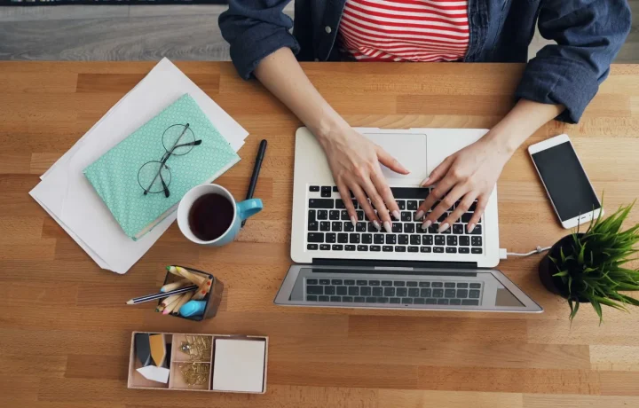 Hands typing on a laptop at a tidy wooden desk, a key step in blog authority building