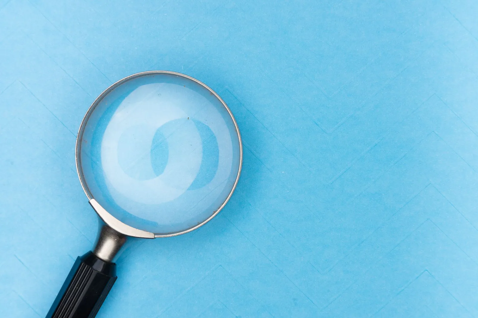 Lupa em uma superfície azul, representando a exploração de temas de pesquisa e palavras-chave no SEO