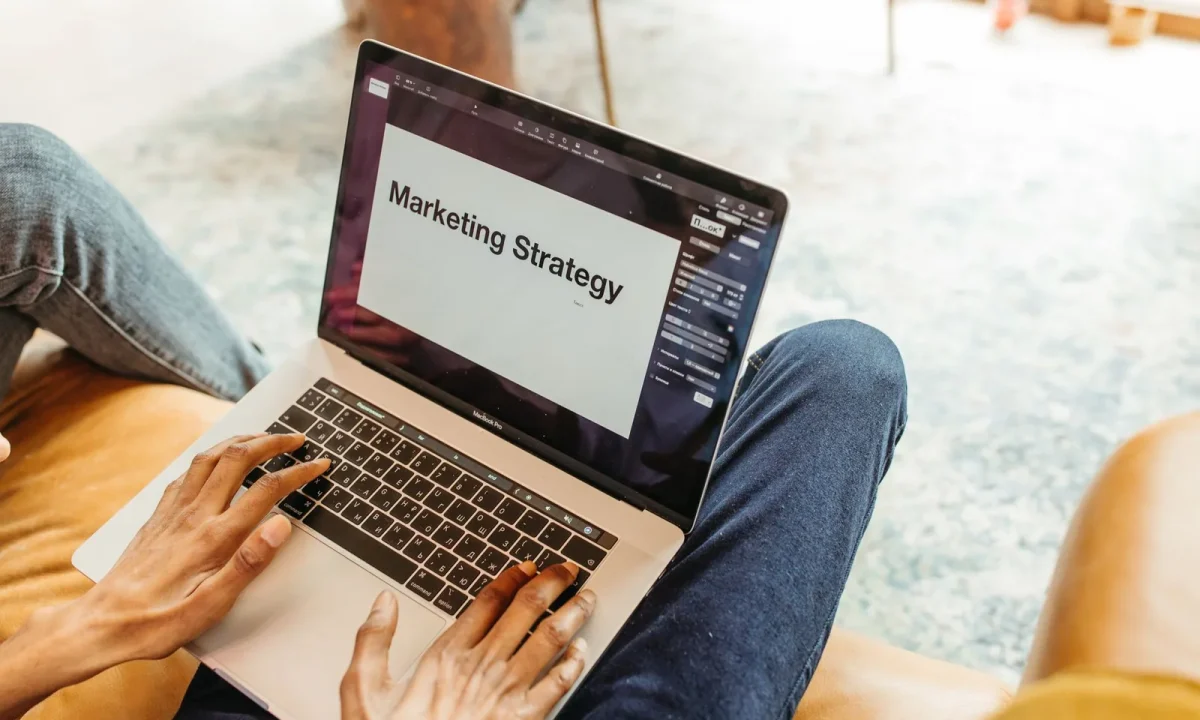 Mãos digitando em notebook com apresentação de estratégia de marketing na tela