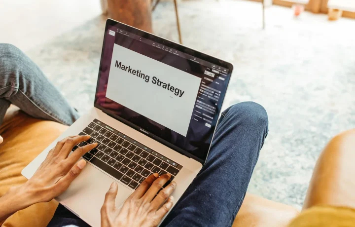 Mãos digitando em notebook com apresentação de estratégia de marketing na tela