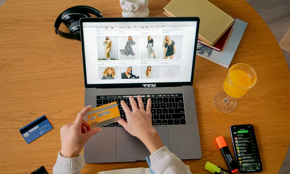 Mãos segurando cartão de crédito para fazer compra online em notebook, ilustrando vendas de produtos digitais