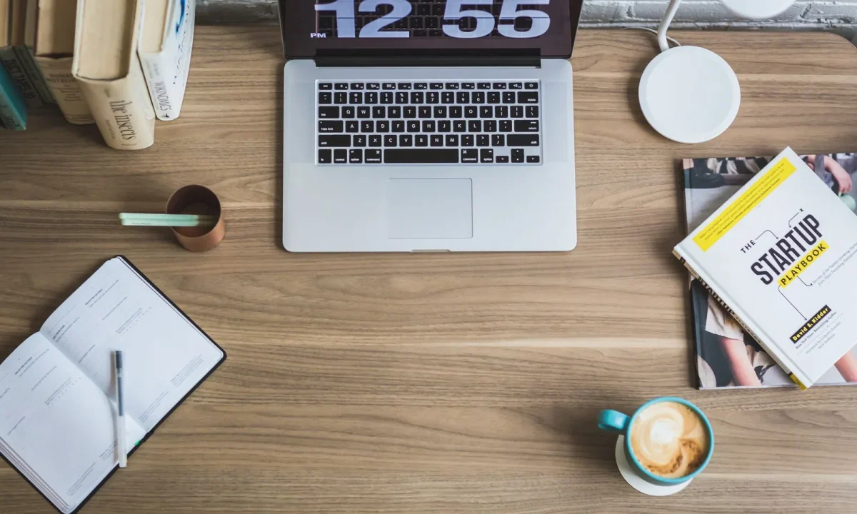 Mesa de madeira com laptop, xícara de café e livros de negócios em composição flat lay, ideal para redes sociais para blogs