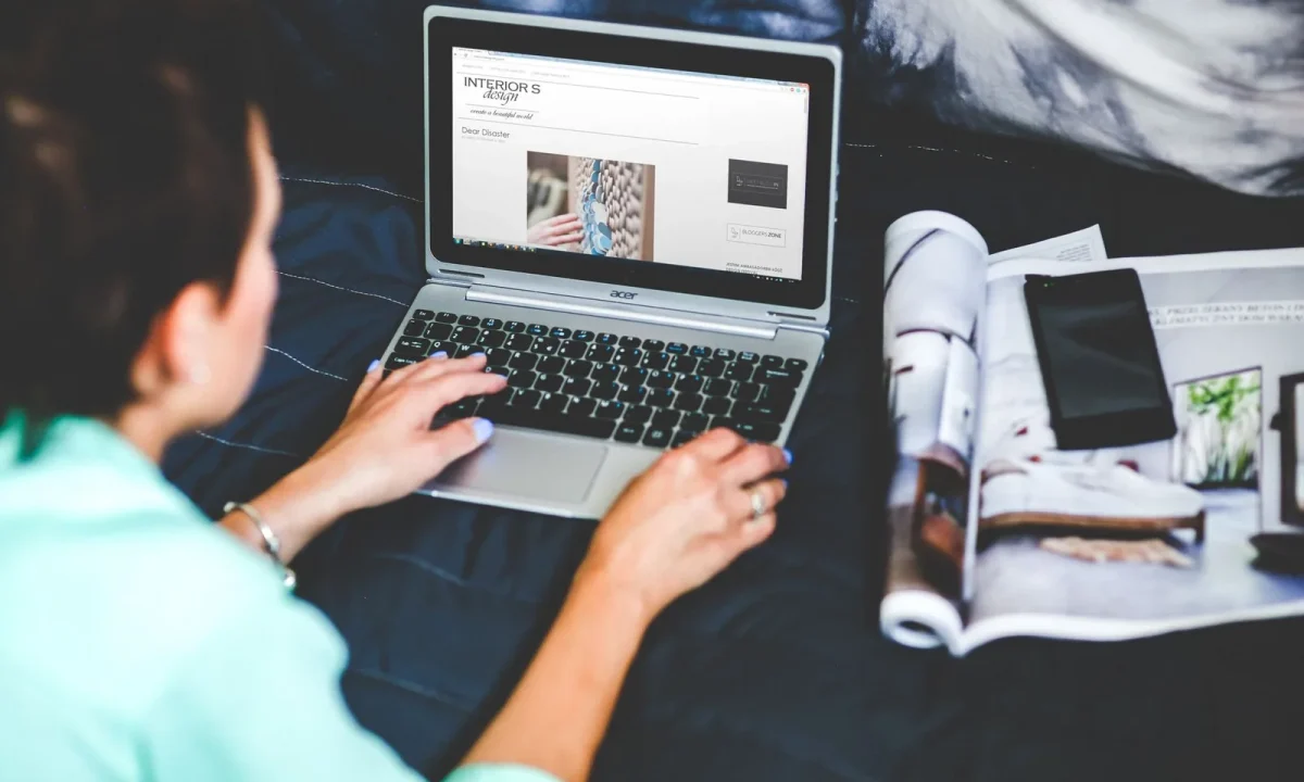 Mulher com notebook e revista na cama, dicas de como evitar conteúdo duplicado em blogs automáticos