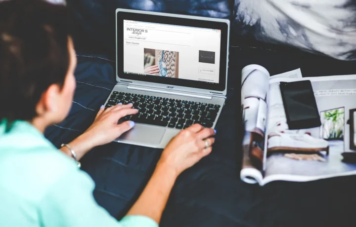 Mulher com notebook e revista na cama, dicas de como evitar conteúdo duplicado em blogs automáticos