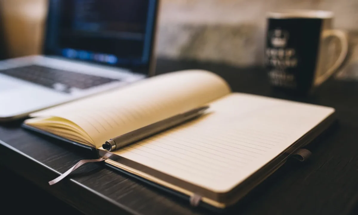 Passo a passo para blog automático com caderno aberto, caneta e notebook sobre mesa de madeira