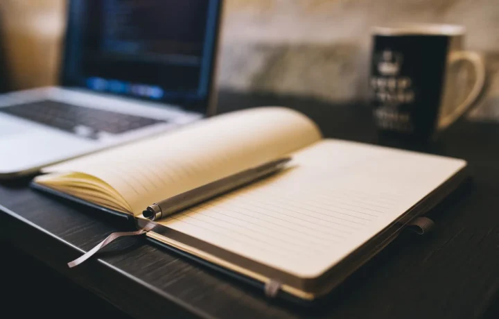Passo a passo para blog automático com caderno aberto, caneta e notebook sobre mesa de madeira
