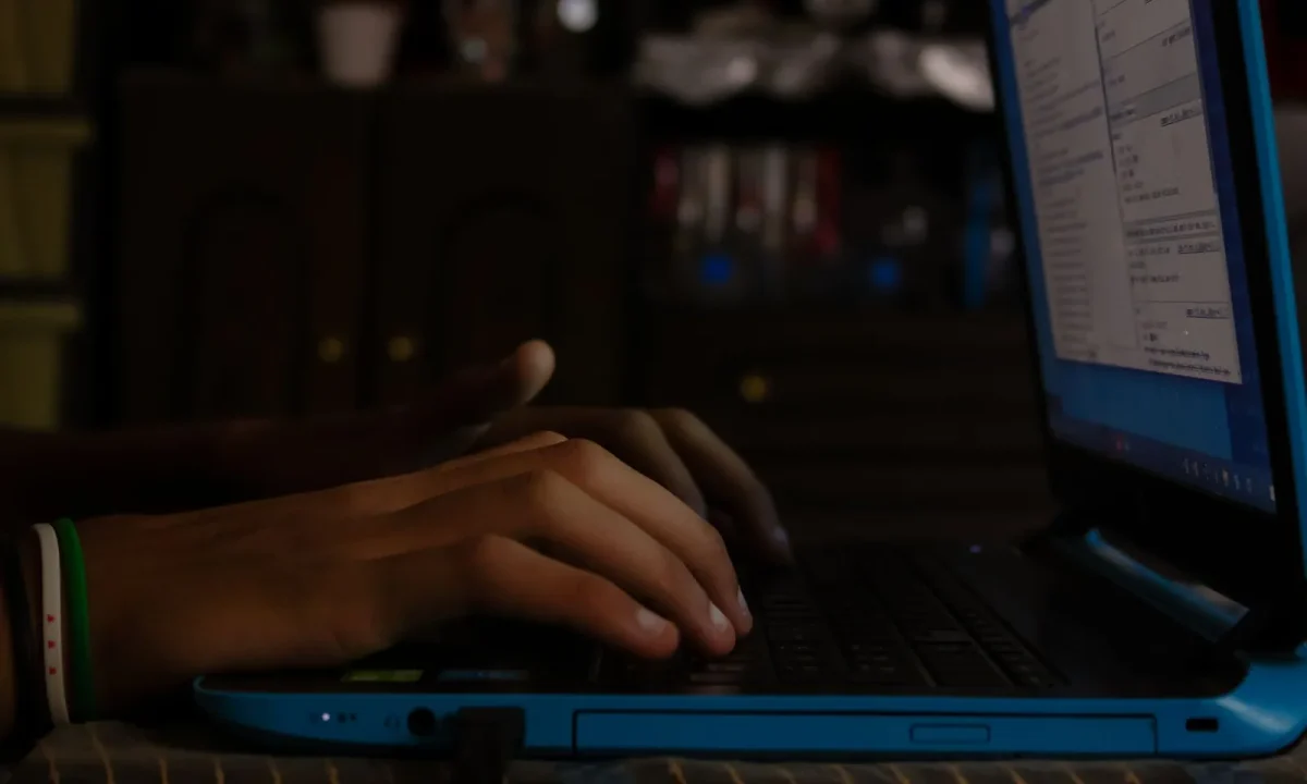 Person typing on a blue laptop while building an automated blog for free in a dimly lit room