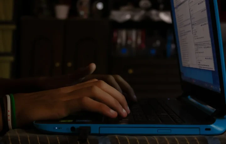 Person typing on a blue laptop while building an automated blog for free in a dimly lit room