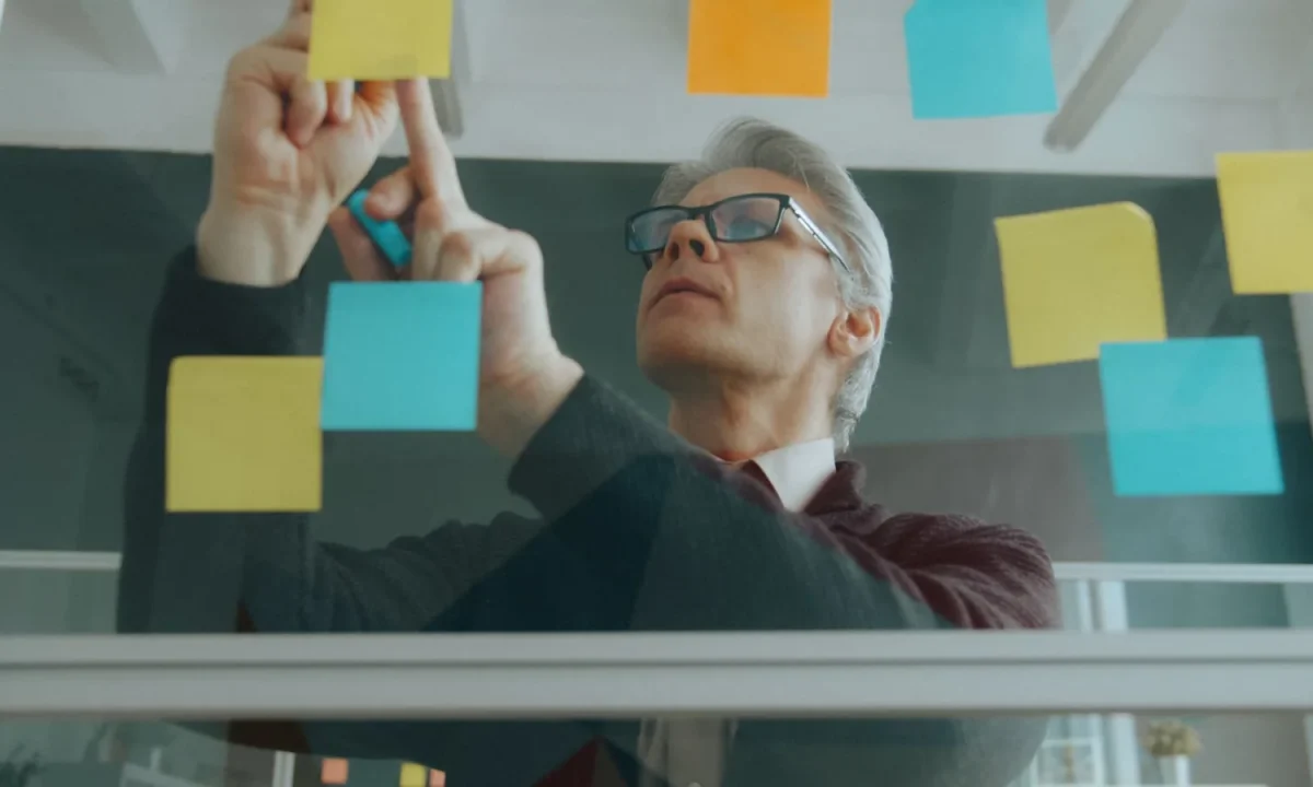 Técnicas de engajamento aplicadas por profissional organizando ideias com post-its em um quadro de vidro