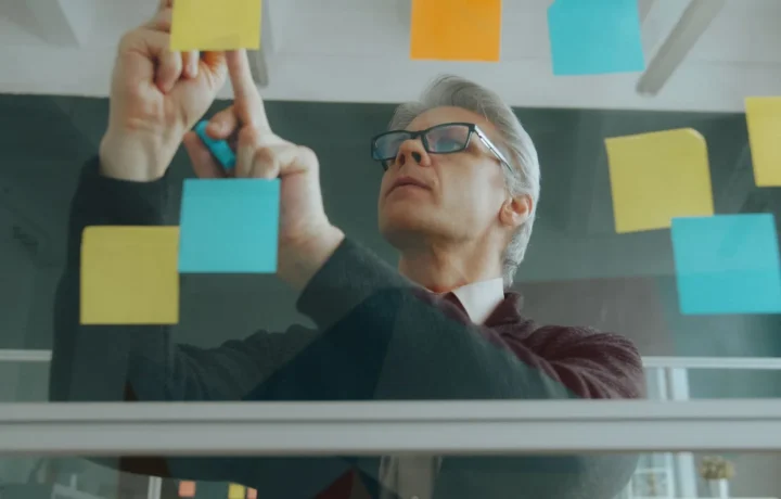Técnicas de engajamento aplicadas por profissional organizando ideias com post-its em um quadro de vidro