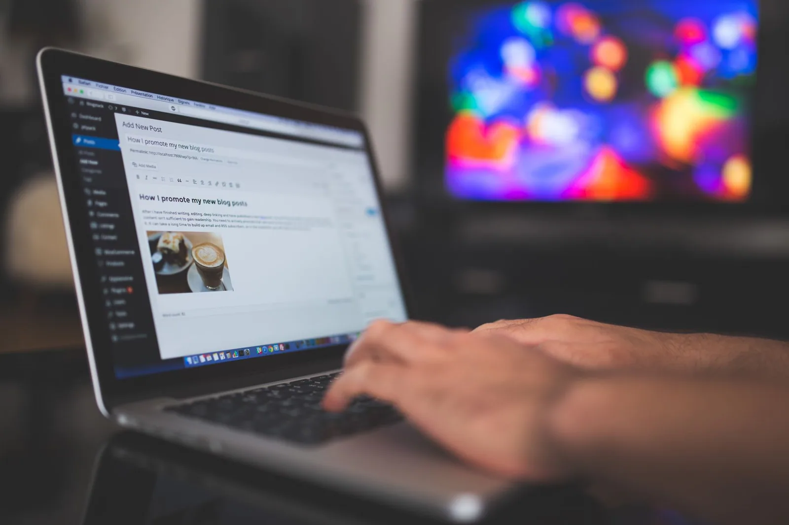 Typing a blog post on a laptop in a cozy room with a colorful screen glowing in the background